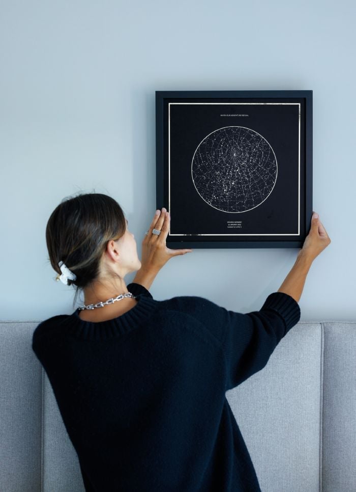 woman hanging star map print on wall