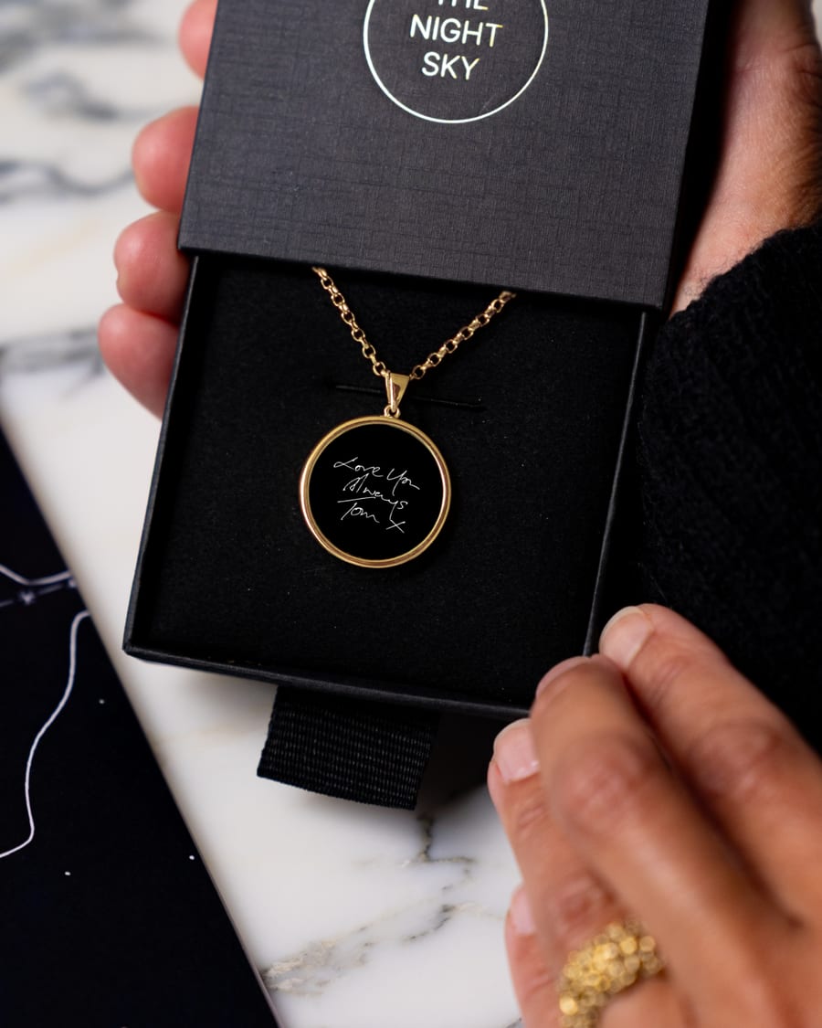 A gold bezel onyx necklace engraved with handwriting, in a Night Sky gift box